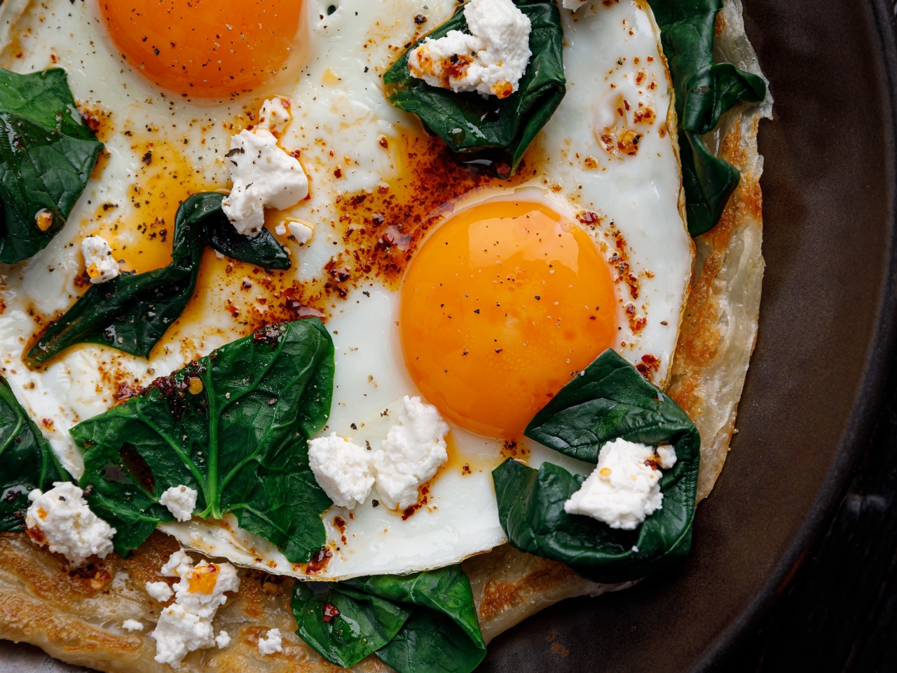 Layered Roti Flatbread with Fried Eggs, Feta Cheese, Sautéed Spinach, and Spicy Oil